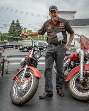 Paul "Flybody" Fedorsak stands between two vintage Harley-Davidson motorcycles with a cigar in his mouth