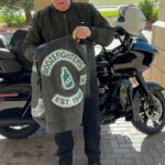 Robert Patrick stands in front of his Harley Davidson Road Glide motorcycle and shows off his perforated Boozefighters vest