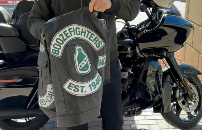Robert Patrick stands in front of his Harley Davidson Road Glide motorcycle and shows off his perforated Boozefighters vest