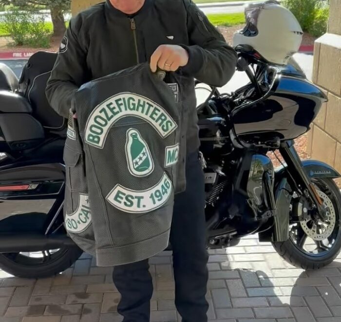 Robert Patrick stands in front of his Harley Davidson Road Glide motorcycle and shows off his perforated Boozefighters vest