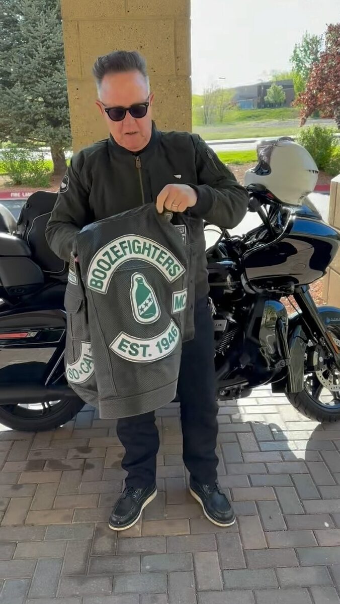 Actor Robert Patrick stands in front of his Harley Davidson Road Glide motorcycle and shows off his perforated Boozefighters vest