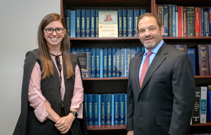 08 Attorneys Christina Gullo and Steve Kantor stand in front of a volume of legal texts with a scale resting on top of the shelves the books sit on.