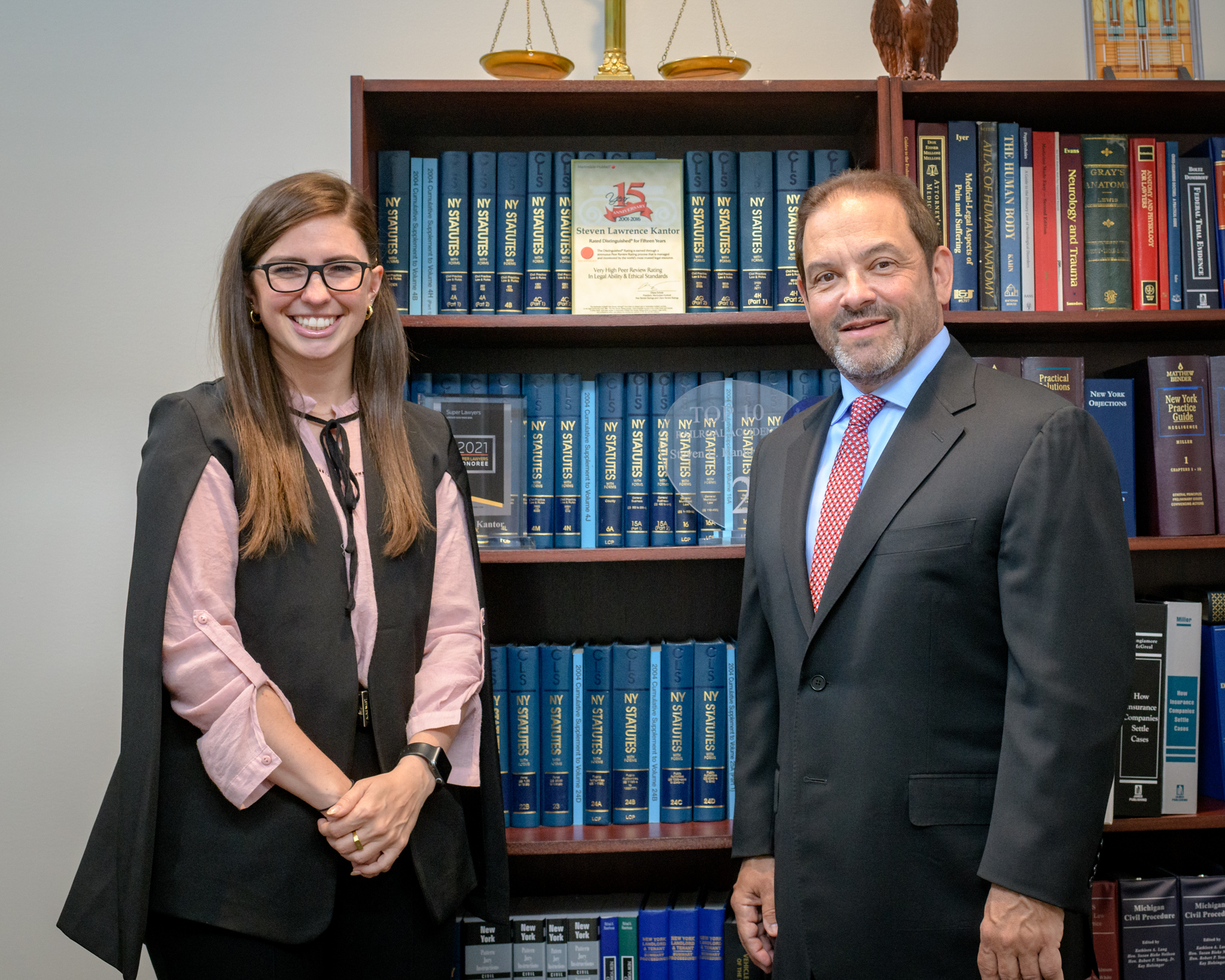 Attorneys Christina Gullo and Steve Kantor stand in front of a volume of legal texts with a scale resting on top of the shelves the books sit on.